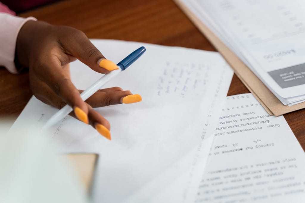 A hand over paperwork at a desk, with pen and writing notes, suggests a busy working environment.