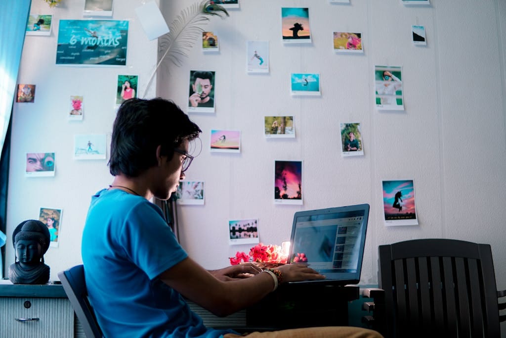 A man working on a laptop in an artistic workspace filled with photos and decor.