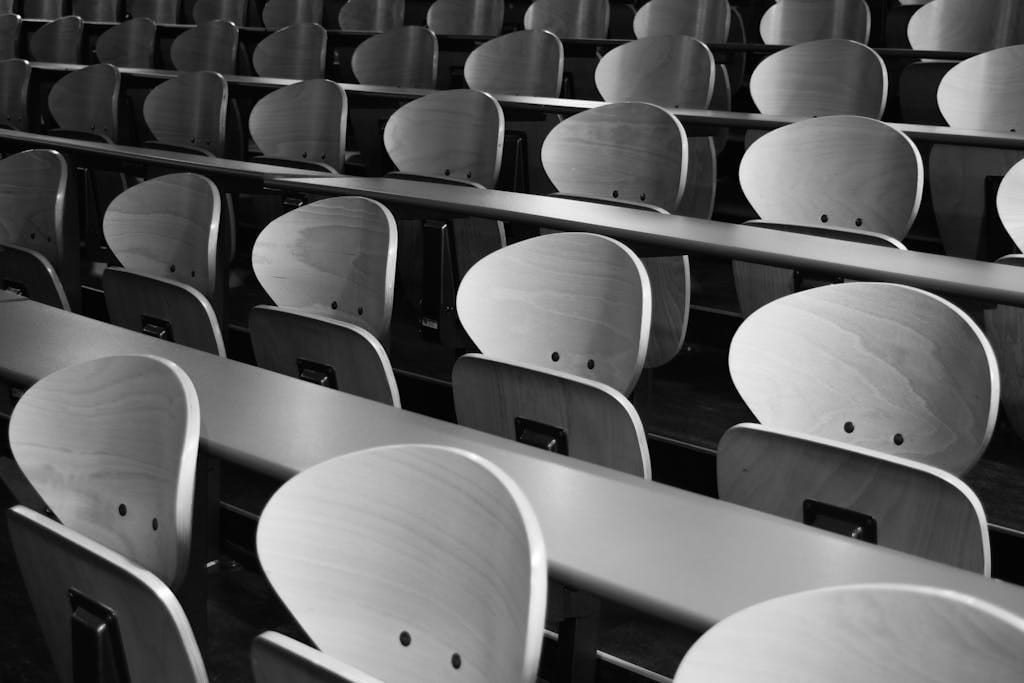 A monochrome view of empty wooden seats in a spacious lecture hall displaying symmetry and design.