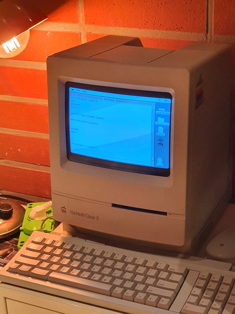 A vintage Macintosh computer with a keyboard under warm indoor lighting, showcasing classic design.
