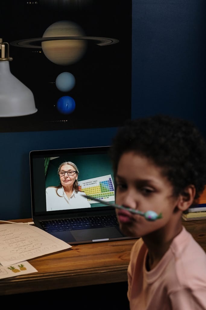Child engaged in an online class with a teacher on a laptop, fostering education.