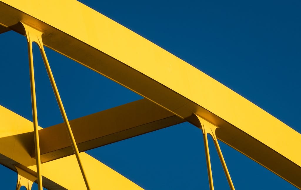 Close-up of yellow bridge arches contrasting with a clear blue sky, showcasing modern architecture.